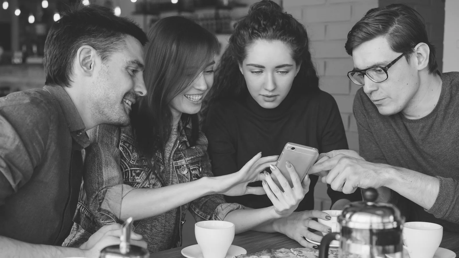 Four friends leaning over one phone at a table, checking an order together